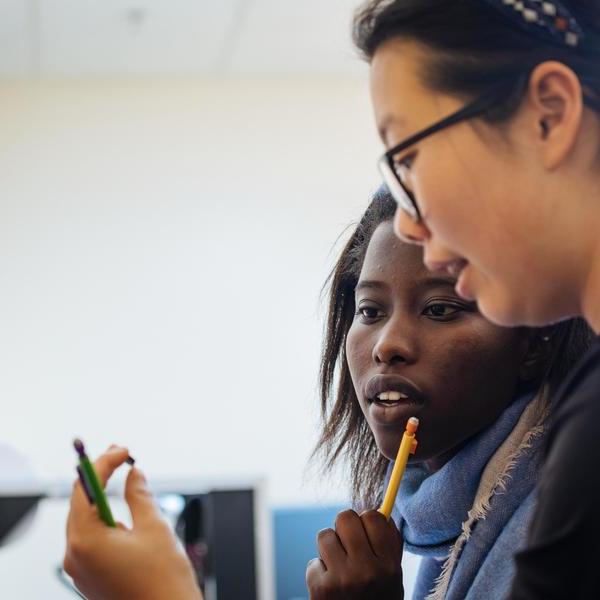 Two Agnes Scott physics major students hold and look closely at a small metal object.